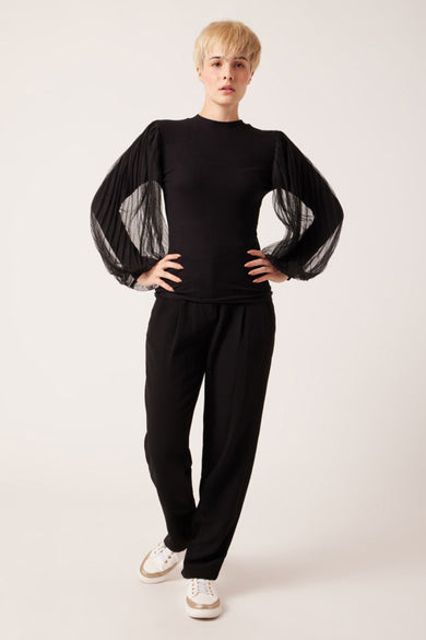 Black ribbed long-sleeve top with sheer pleated sleeves, full-length front view on model wearing black trousers and white sneakers