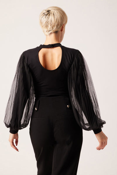 Black ribbed long-sleeve top with sheer puffed sleeves and open back, worn with black high-waisted pants, back view