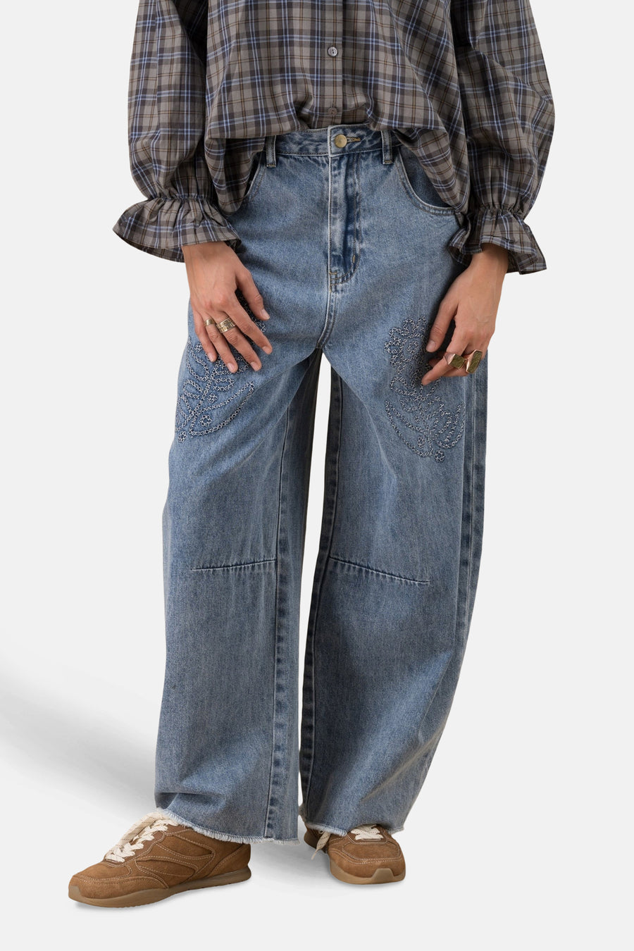 Jean en denim bleu clair par ADORE, avec broderies décoratives et porté avec une chemise à carreaux et des baskets marron.
