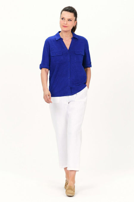 Blauwe blouse met korte mouwen van CAROLL, gedragen met een witte broek en bruine loafers.