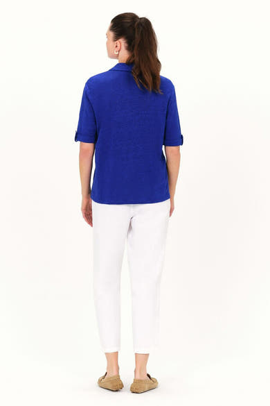 Chemise à manches courtes bleue de CAROLL, portée avec un pantalon blanc et des mocassins beiges, vue de dos.
