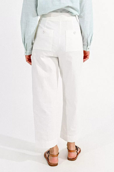 Pantalon coloré blanc de Molly Bracken, avec poches plaquées boutonnées à l'arrière, porté avec une chemise rayée et des sandales en cuir.