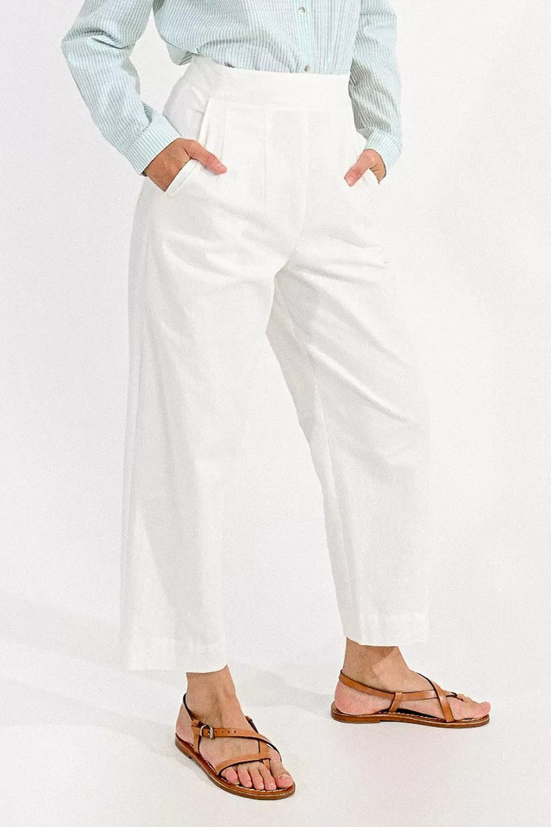 Pantalon coloré blanc par Molly Bracken, avec des poches et une coupe ample, porté avec une chemise rayée et des sandales.