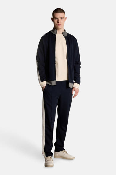 Beige T-shirt met korte mouwen van Lyle & Scott, gedragen met een trainingsjack en een marineblauwe joggingbroek.