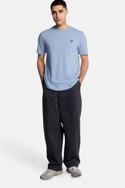 T-shirt bleu à manches courtes de LYLE & SCOTT, porté avec un pantalon noir ample et des baskets grises.