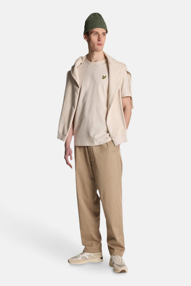 Beige T-shirt met korte mouwen van LYLE & SCOTT, gedragen met een groene muts en een beige vest over de schouders.