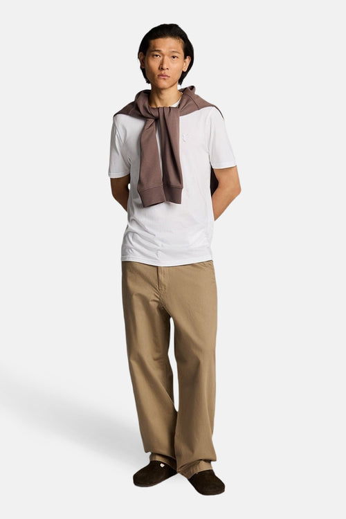 T-shirt à manches courtes blanc de LYLE & SCOTT, porté avec un pull noué sur les épaules et un pantalon beige ample.