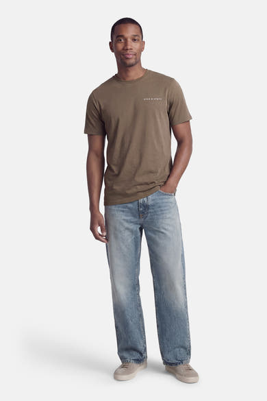T-shirt kaki à manches courtes de LYLE & SCOTT, porté avec un jean bleu délavé et des chaussures de sport grises.