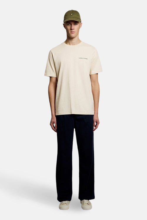 T-shirt à manches courtes écru de LYLE & SCOTT, porté avec un pantalon ample et une casquette.