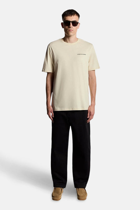 Beige T-shirt met korte mouwen van Lyle & Scott, gedragen met een zwarte wijde broek en bruine loafers.