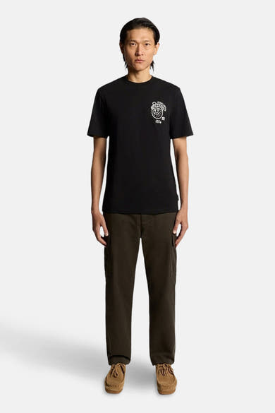 T-shirt à manches courtes bleu foncé de LYLE & SCOTT, avec un motif imprimé blanc sur la poitrine, porté avec un pantalon cargo et des chaussures marron.