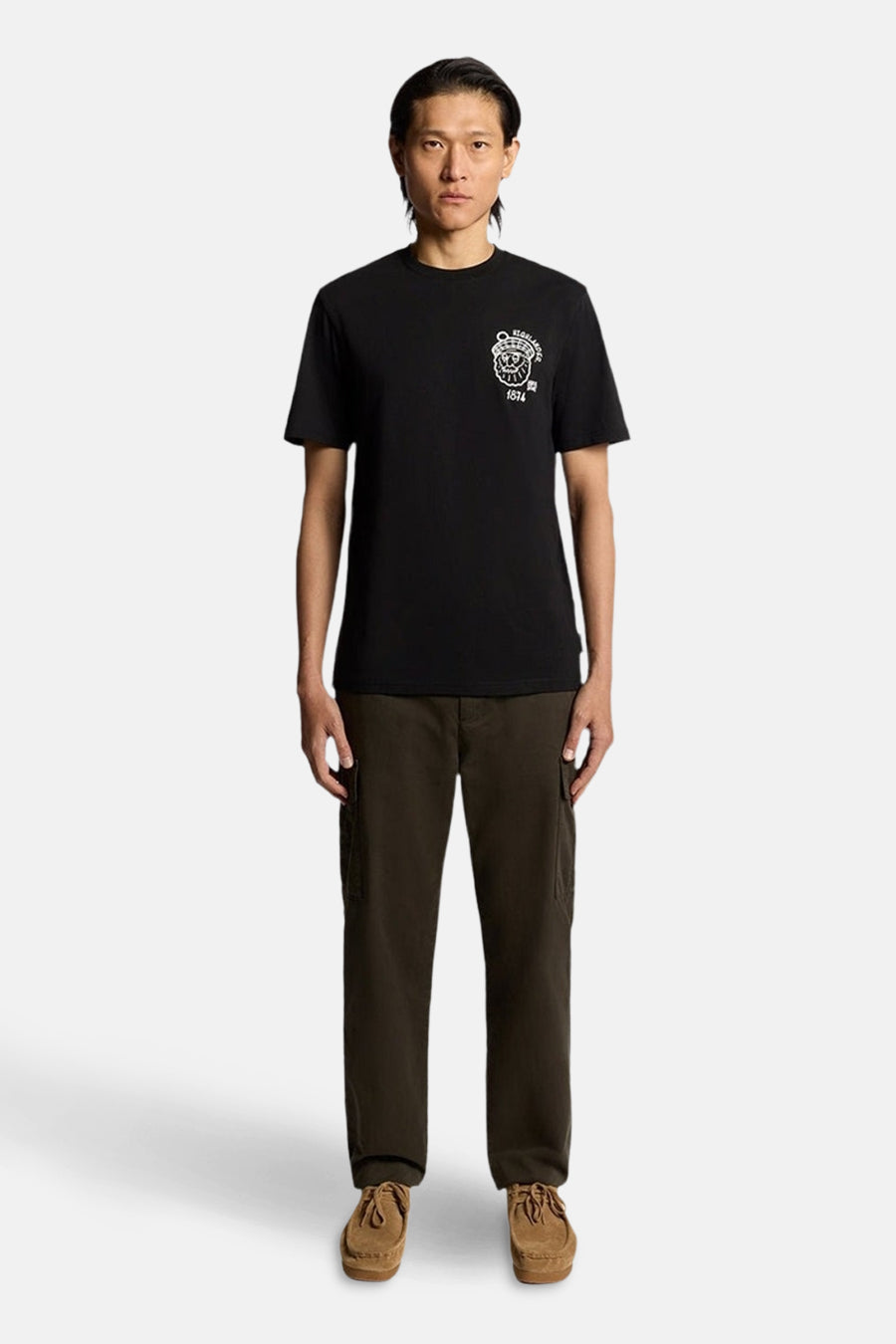 T-shirt à manches courtes bleu foncé de LYLE & SCOTT, avec un motif imprimé blanc sur la poitrine, porté avec un pantalon cargo et des chaussures marron.