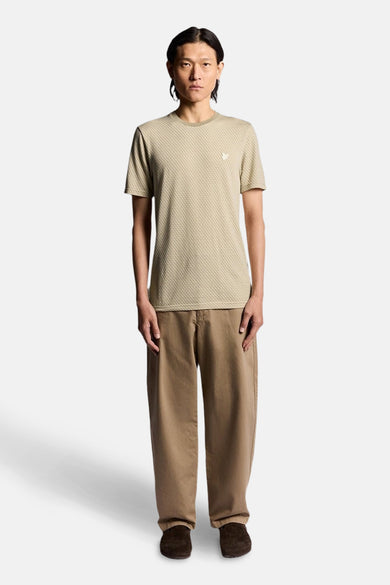 T-shirt beige à manches courtes de LYLE & SCOTT, motif tissé discret, porté avec un pantalon marron ample.