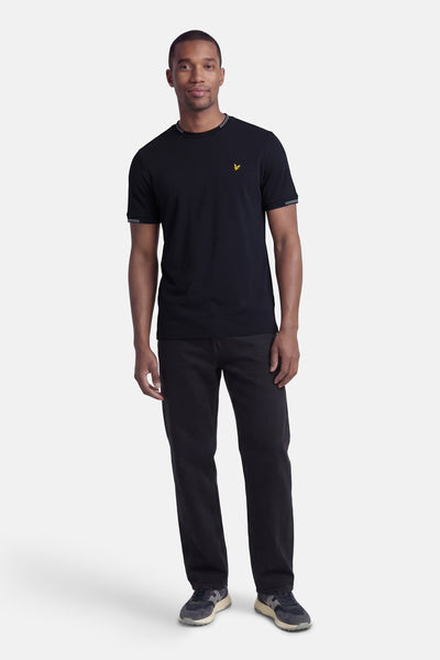 T-shirt à manches courtes bleu de LYLE & SCOTT avec logo jaune, porté avec un pantalon noir et des baskets.