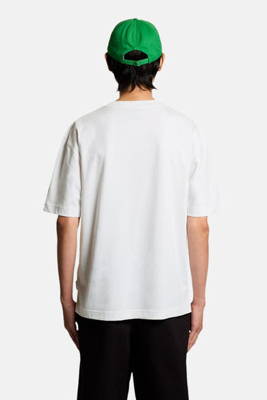 T-shirt blanc de LYLE & SCOTT, vue de dos, porté avec une casquette verte et un pantalon noir.