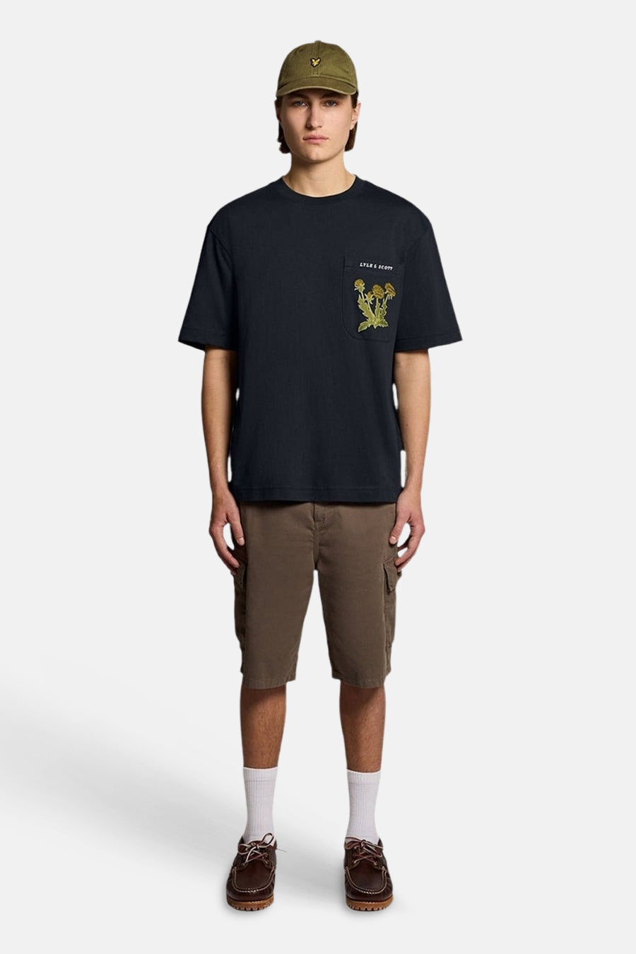 Ruim marineblauw T-shirt van LYLE & SCOTT met geborduurde bloemenprintzak, gedragen met een bruine cargoshort en een kaki pet.