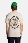 Ecru T-shirt van LYLE & SCOTT met kleine kleurrijke bloemenprint op de borst, gedragen met wijde broek en groene pet.