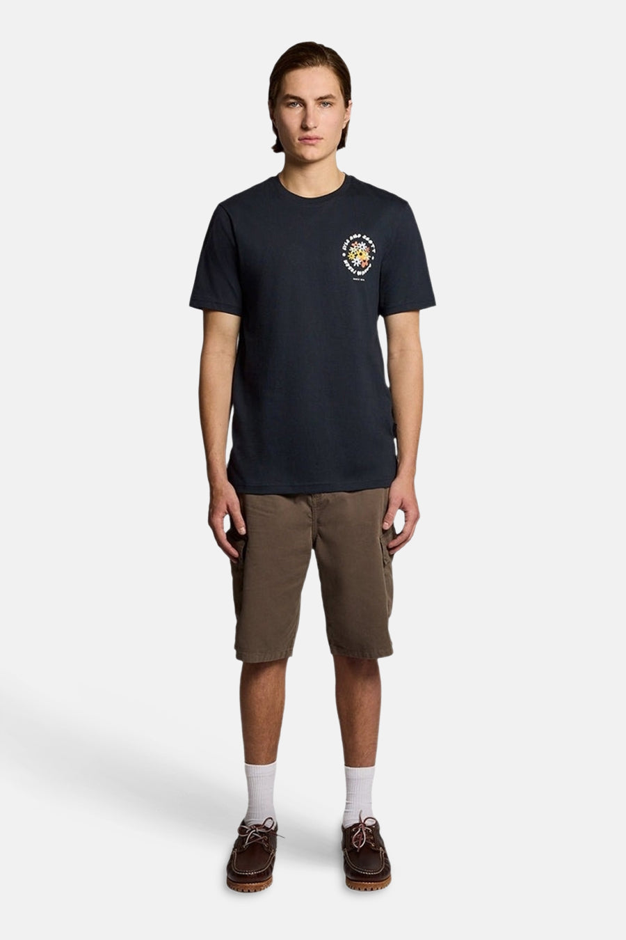 T-shirt bleu de LYLE & SCOTT avec motif circulaire coloré sur la poitrine, porté avec un short cargo marron et des chaussures bateau.