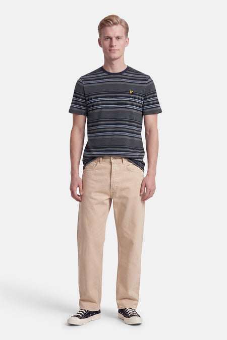 T-shirt à manches courtes multicolore rayé par LYLE & SCOTT, col rond, logo brodé jaune, porté avec pantalon beige et baskets noires