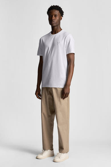 T-shirt à manches courtes blanc de LYLE & SCOTT, porté avec un pantalon chino beige et des baskets blanches.