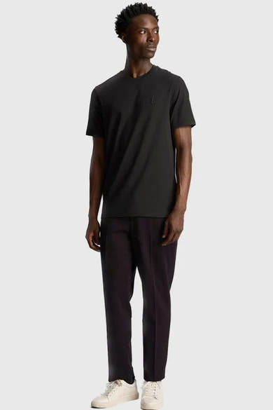 T-shirt noir à manches courtes de Lyle & Scott, porté avec un pantalon foncé et des baskets blanches.