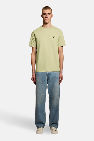 T-shirt à manches courtes vert olive de Lyle & Scott, porté avec un jean bleu et des baskets beiges.
