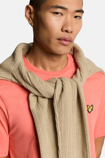 T-shirt à manches courtes corail de LYLE & SCOTT, avec un pull en tricot torsadé clair noué sur les épaules.
