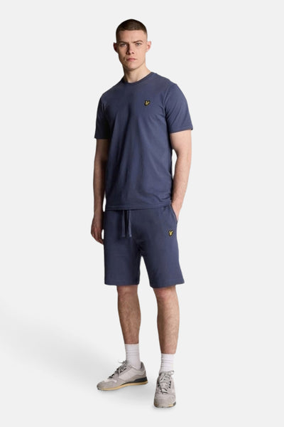 T-shirt bleu à manches courtes de LYLE & SCOTT, porté avec un short assorti, des chaussettes blanches et des baskets grises.