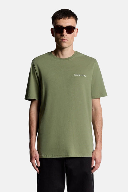 Olijfgroen T-shirt met korte mouwen van Lyle & Scott, gedragen met een zwarte broek en een bruine zonnebril.