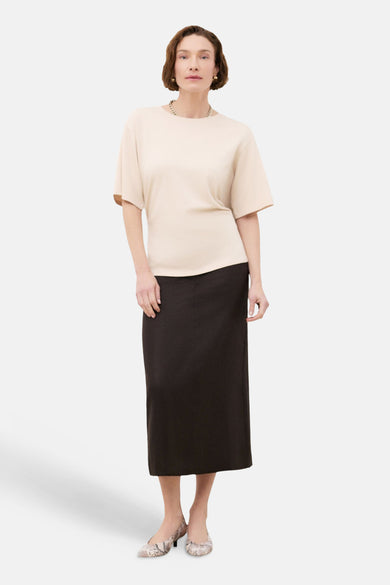 Beige T-shirt van CAROLL, korte mouwen, gedragen met een zwarte rok en bedrukte schoenen.
