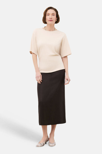 Beige T-shirt van CAROLL, korte mouwen, gedragen met een zwarte rok en bedrukte schoenen.