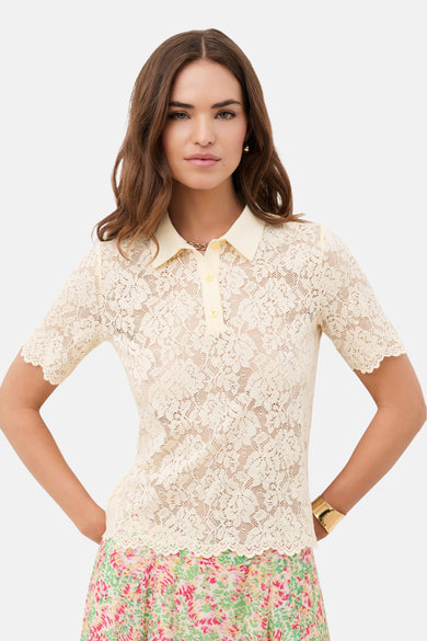 Polo jaune de CAROLL en dentelle, à manches courtes et col classique, porté avec une jupe fleurie.