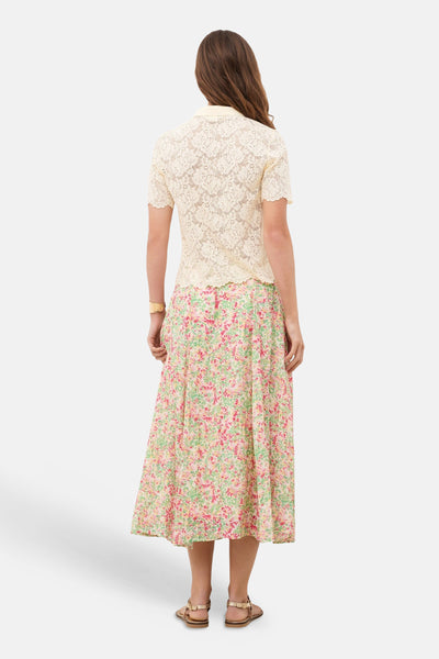 Polo jaune de CAROLL en dentelle à manches courtes, porté de dos avec une jupe fleurie.
