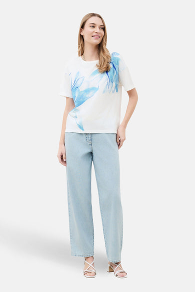 T-shirt à manches courtes blanc de CAROLL, avec imprimé floral bleu sur le devant, porté avec un jean taille haute.
