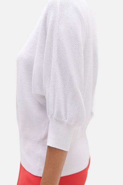 Witte Caroll trui met driekwart pofmouwen, textuur breisel, gedragen met een rode broek, zijaanzicht.