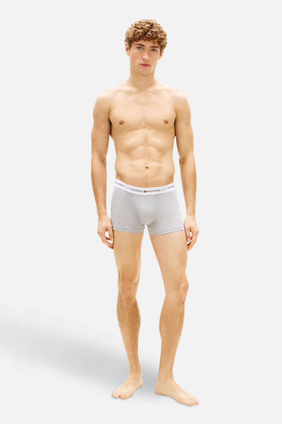 Boxer gris de Tommy Jeans, porté par un homme torse nu et musclé, debout devant un fond blanc.