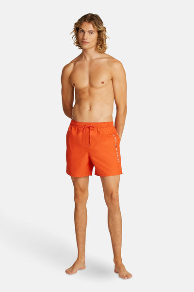Oranje zwembroek van TOMMY HILFIGER, gedragen door een man met blond haar, handen achter zijn rug gevouwen.