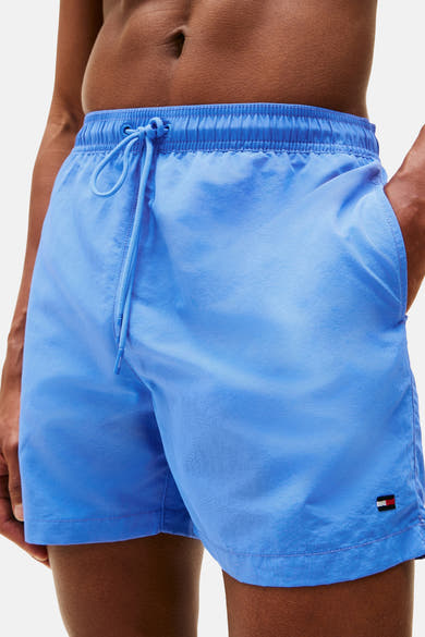 Blauwe zwembroek van Tommy Hilfiger gedragen met een open wit overhemd en een strandtas.
