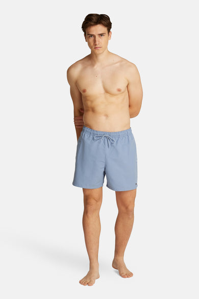 Blauwe zwembroek van Tommy Hilfiger, gedragen door een model zonder shirt, met de handen achter de rug.