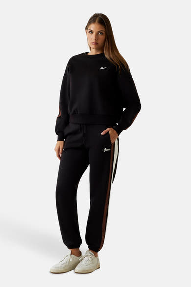 Zwarte joggingbroek van Guess met een bruine en witte streep aan de zijkant, gedragen met witte sneakers.