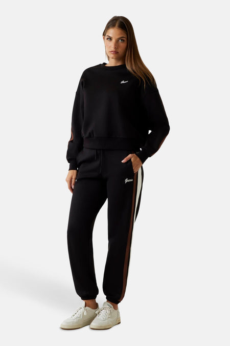Zwarte joggingbroek van Guess met een bruine en witte streep aan de zijkant, gedragen met witte sneakers.
