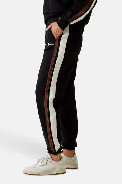Zwarte joggingbroek van Guess met bruine en witte strepen aan de zijkant en geborduurd logo.