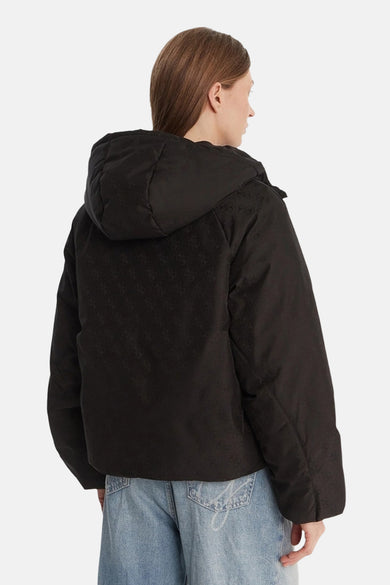 Veste courte noire par Guess, avec motif imprimé ton sur ton et capuche, portée avec un jean bleu clair.
