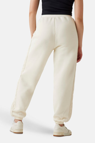 Jogging écru de Guess, avec un bordure à motif logo et ourlet élastique, porté avec un top noir.