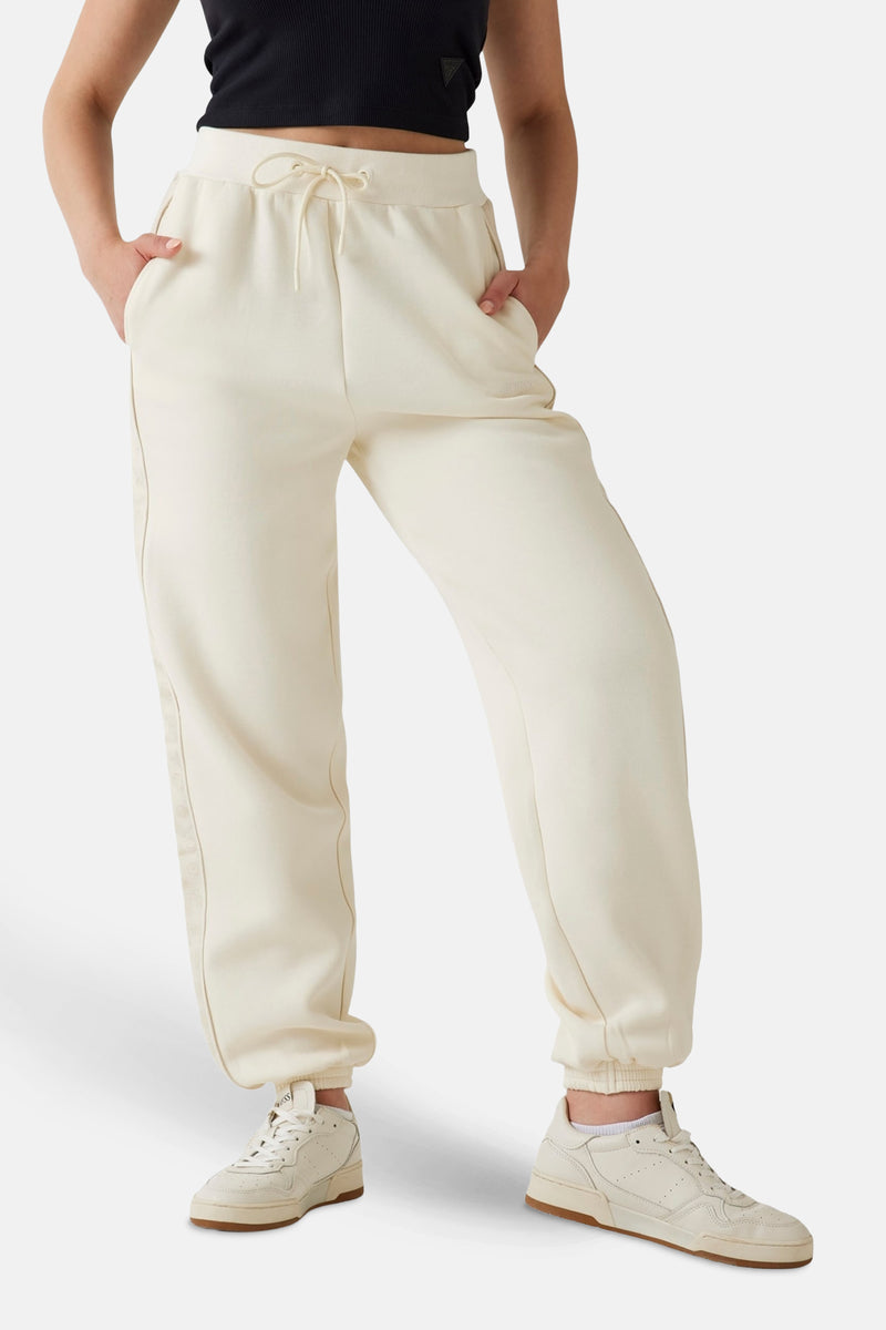 Jogging écru de Guess, avec cordon de serrage à la taille, porté avec un haut noir et des baskets blanches.