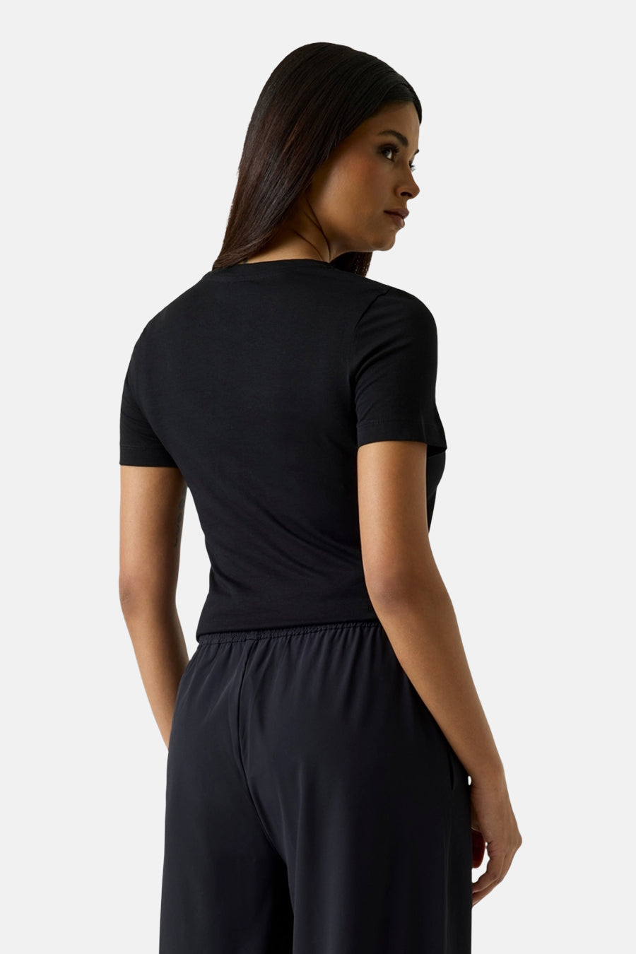 T-shirt noir à manches courtes de Guess®, porté de dos par une femme avec un pantalon noir.