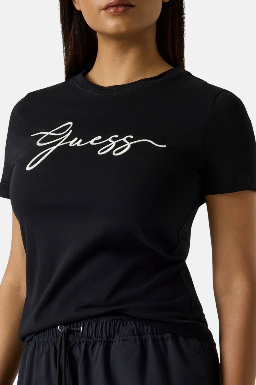 T-shirt noir à manches courtes de Guess avec le logo blanc en écriture cursive, porté avec un pantalon à cordon.