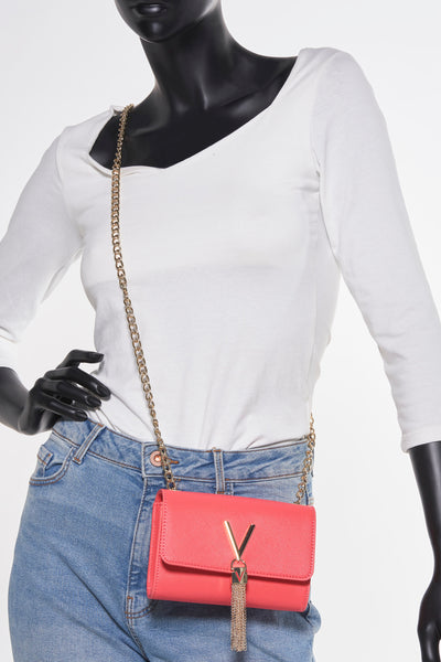 Sac à bandoulière rose de VALENTINO BAGS avec chaîne dorée et finitions à glands, porté avec un jean.
