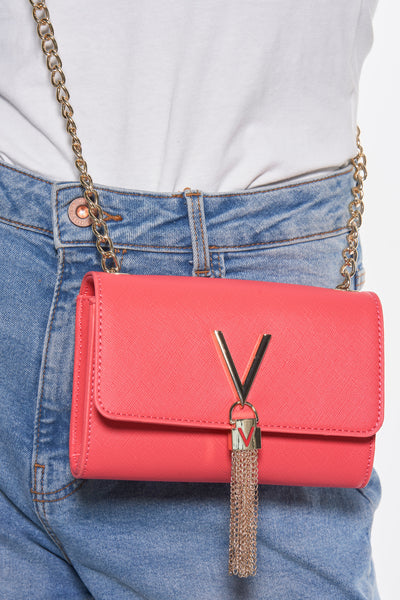 Sac à bandoulière rose de VALENTINO BAGS avec chaîne dorée et détails décoratifs dorés, porté avec un t-shirt blanc et un jean.
