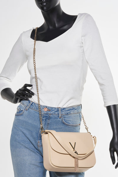 Sac à bandoulière écru de VALENTINO BAGS avec bandoulière chaîne dorée, porté avec un jean bleu et un haut blanc.